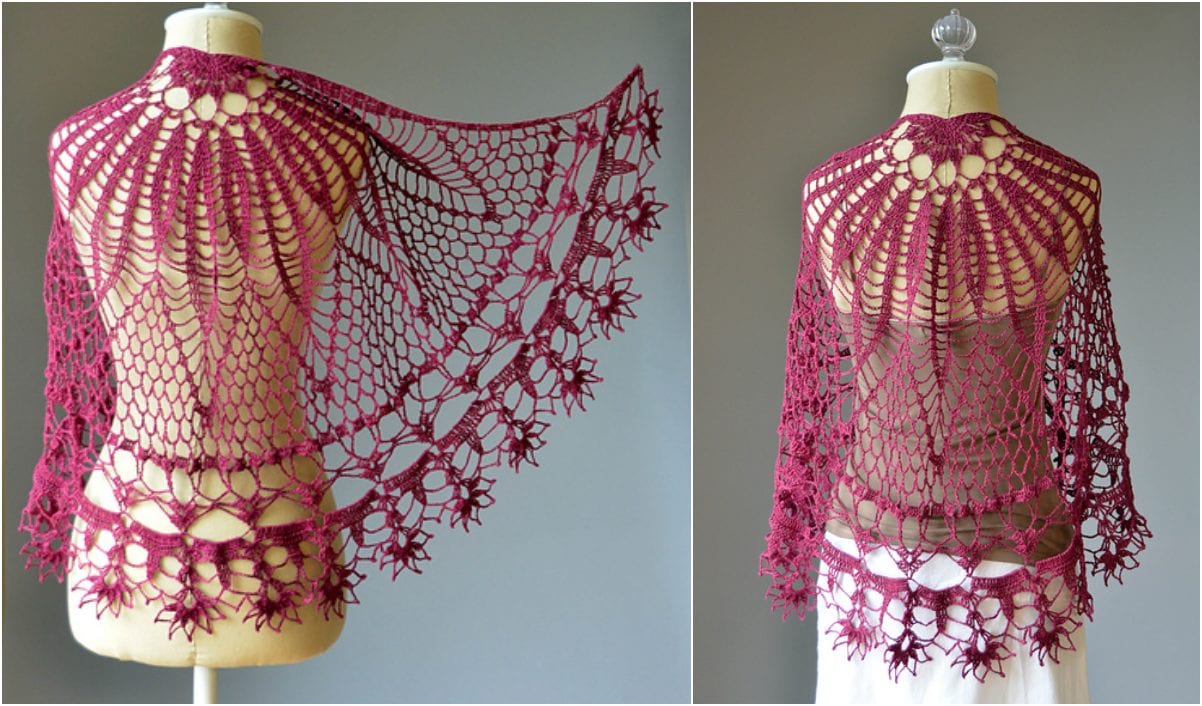 A crochet shawl in a deep red color is displayed on a mannequin, showcasing intricate lace patterns reminiscent of a Ragdoll Crochet style and a charming floral edge design.