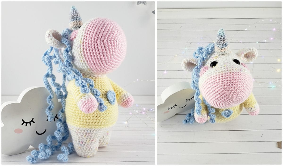 A crocheted unicorn toy with blue curly hair, a pink snout, and a yellow body stands on a white wooden surface next to a cloud decoration, inspiring thoughts of crafting your own with a free crochet pattern.