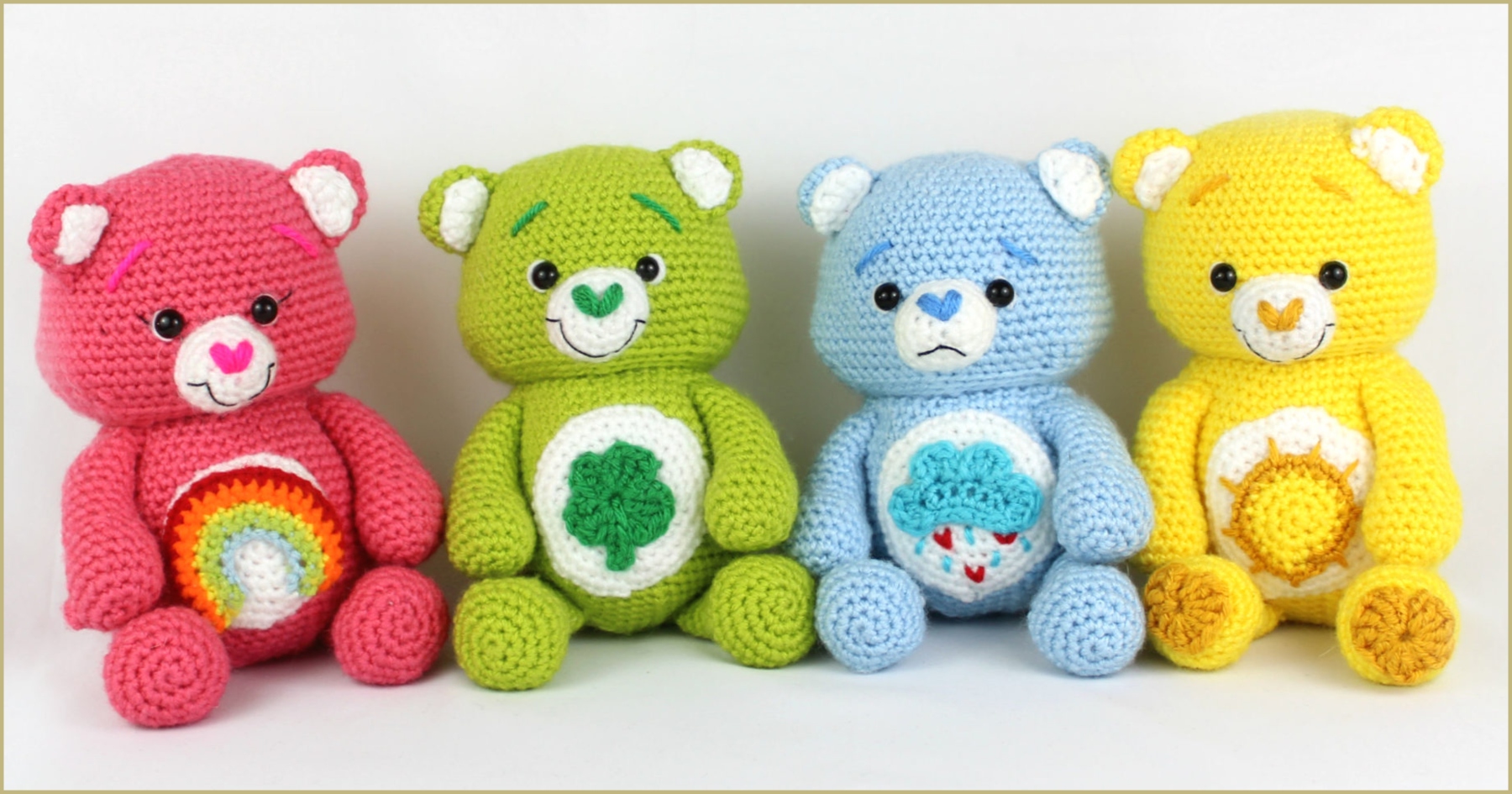 Introducing the Happy Bears collection: four crocheted teddy bears in pink, green, blue, and yellow. Each bear showcases a unique emblem on its belly—a rainbow, clover, cupcake, and sun—crafted from a free crochet pattern perfect for your next creative project.