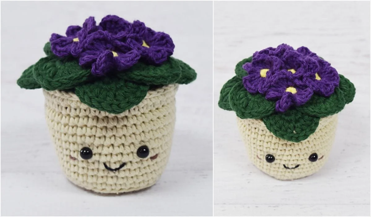 Crocheted plush resembling a potted plant with green leaves, African violet flowers, and a smiling face.