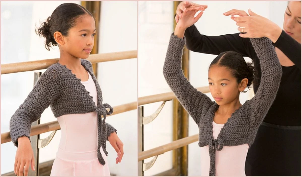 A ballet instructor adjusts a young dancer's arm position. The dancer, clad in a pink leotard and gray knitted wrap with a delicate crochet pattern, stands poised at the barre.