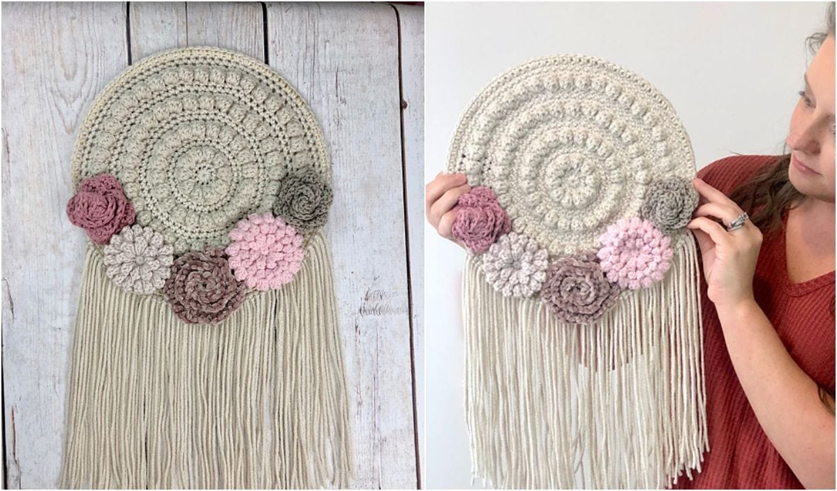 A woman holds a crocheted wall hanging, reminiscent of a Lake Sunset Shawl, adorned with fringe and floral accents in shades of pink and gray.