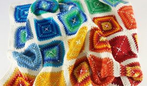 This crocheted blanket, featuring a vibrant diamond pattern in blue, green, yellow, orange, and red with white borders, can be created using the free crochet pattern from the Miarly CAL.