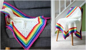 A white knitted blanket with rainbow edges and a subtle crochet pattern is draped over a gray couch and a wooden chair near the stairs.