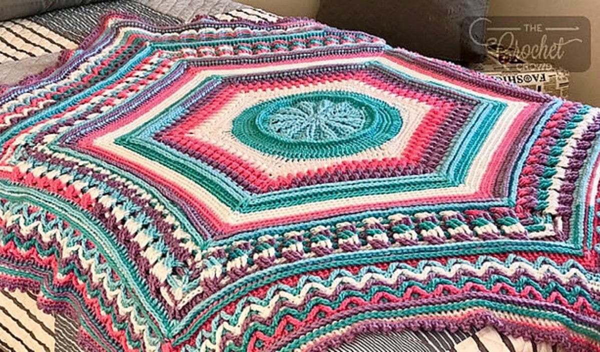 A colorful crochet blanket with intricate hexagonal patterns and various shades of pink, teal, and purple, beautifully displayed on a bed. Perfect for adding warmth and style to any room.