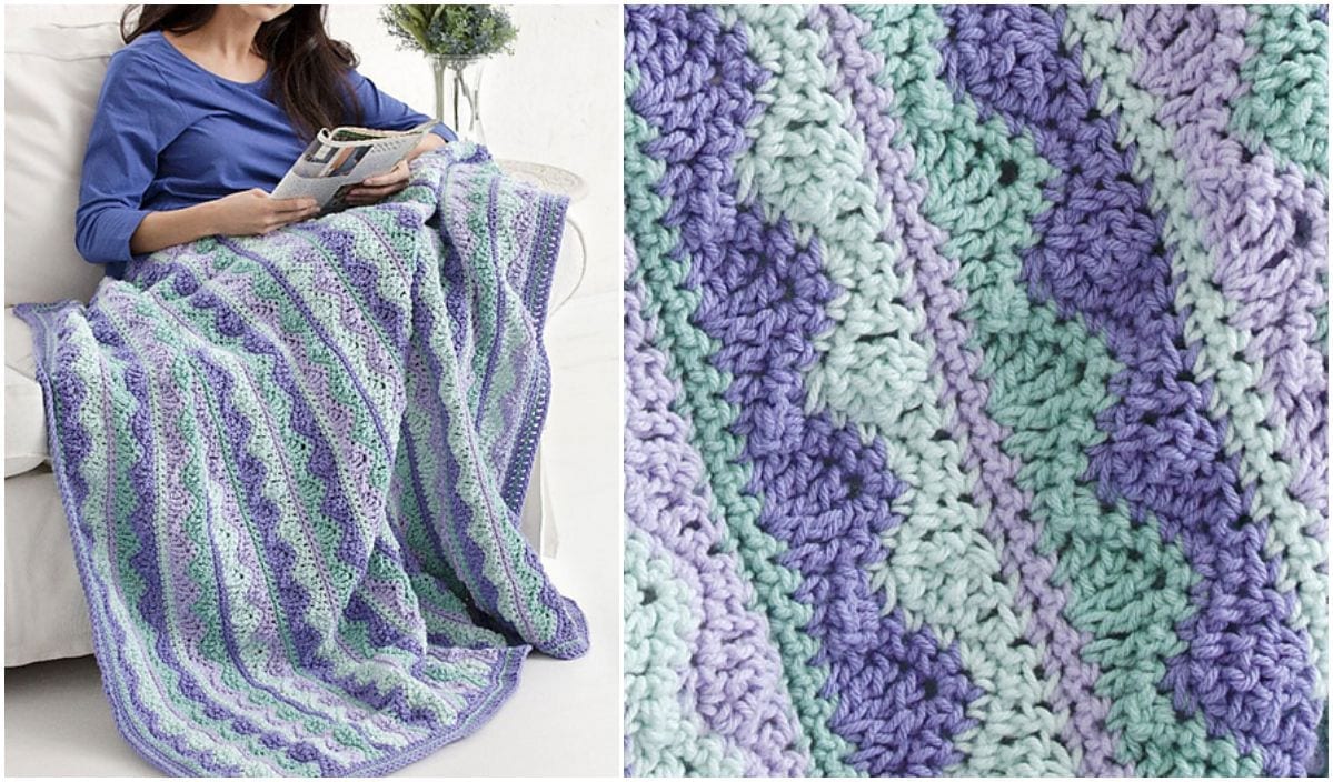 A person is wrapped in a crocheted blanket featuring the Miarly CAL pattern with purple, green, and white designs, while reading a book. The close-up reveals the intricate stitch work of the blanket.