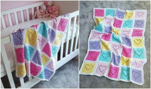 A crocheted blanket with colorful heart squares is draped over a white crib, its charming crochet patterns complementing the nursery. Nearby, enjoy a full view of the blanket on a gray carpet, perfect for those seeking inspiration for their next creation.