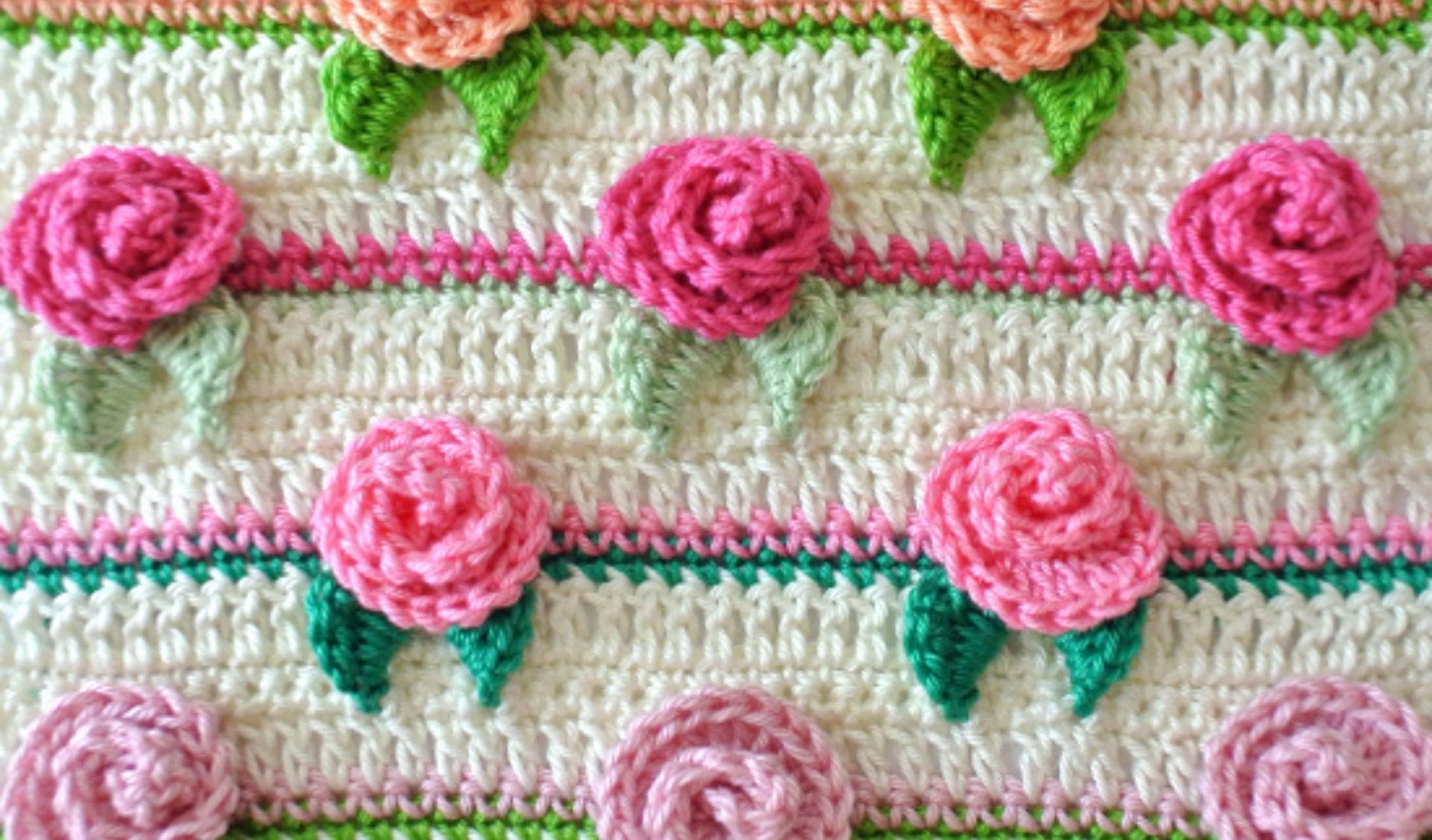 Crochet pattern featuring rows of pink and peach rose designs with green leaves on a cream background, reminiscent of a whimsical mermaid doll's garden.