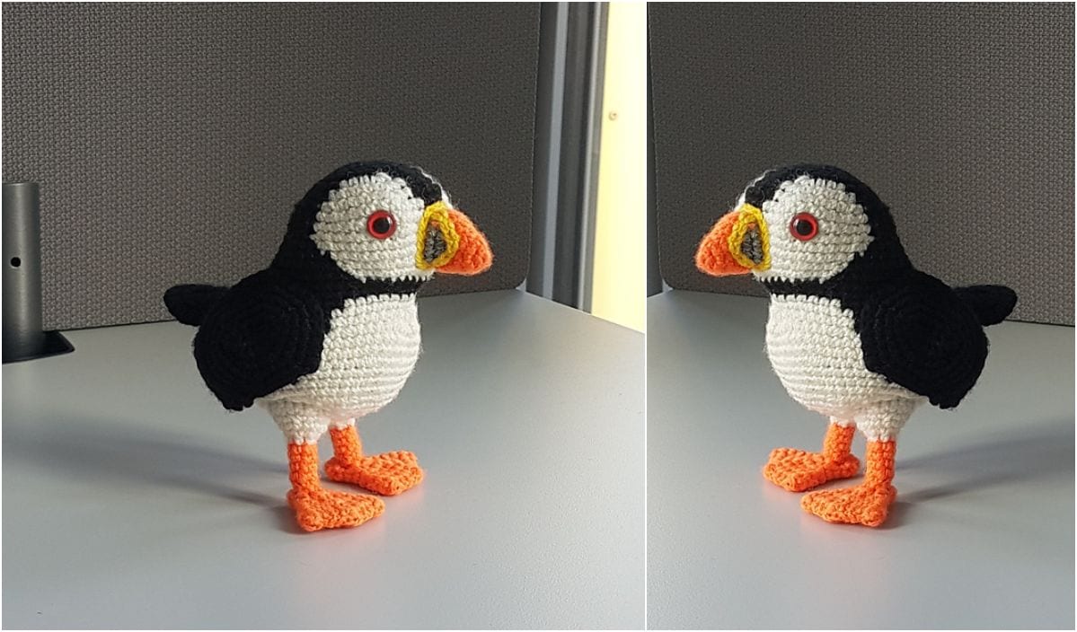 A crocheted puffin in black, white, and orange stands proudly on a gray surface, showcasing its charm from two angles. This delightful creation is a perfect example of exotic amigurumi animals.