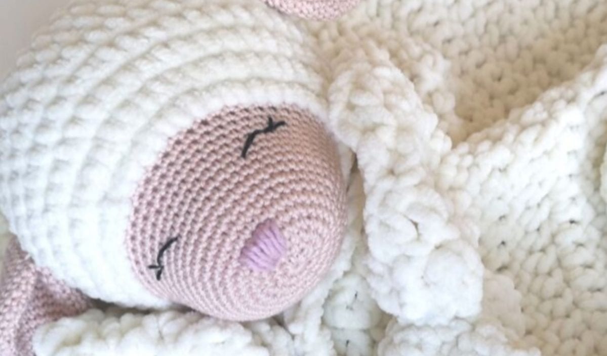 A crocheted stuffed toy in the shape of a sleeping baby, wrapped snugly in a white knitted blanket, is an adorable creation straight from imaginative crochet patterns.