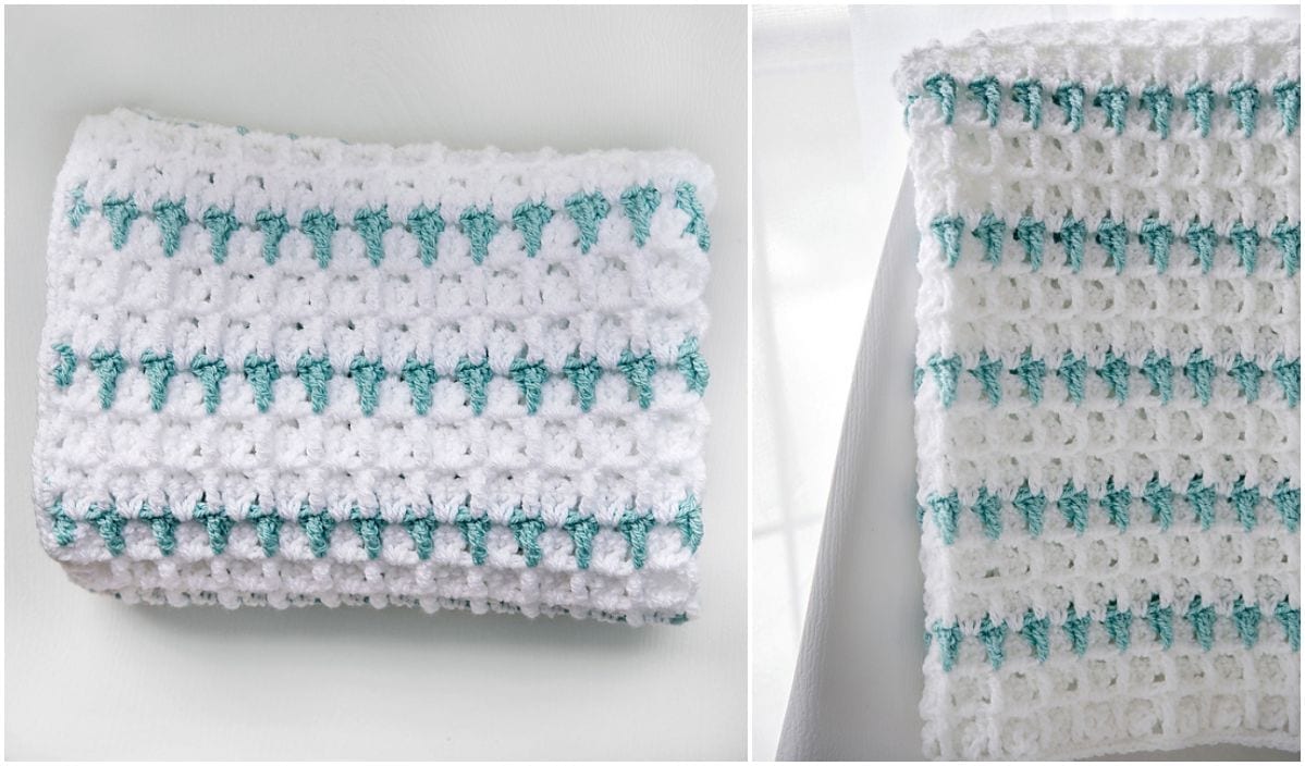 A crocheted white baby blanket with teal lines folded on a white surface. The close-up showcases the texture and intricate crochet patterns.