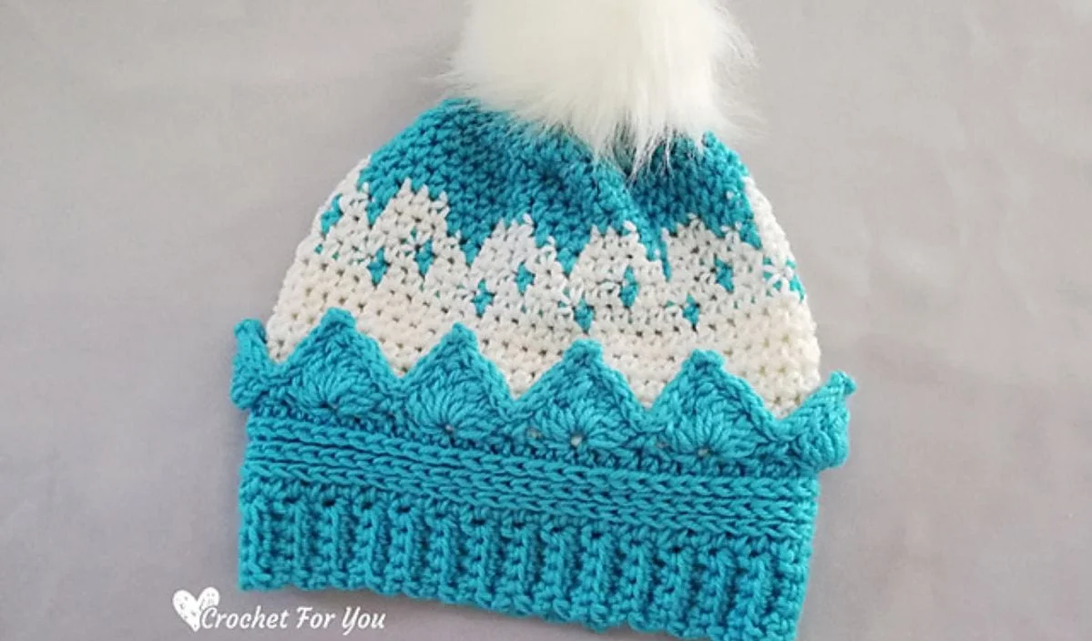 Crocheted beanie with turquoise and white zigzag pattern, a white fluffy pom-pom on top, and perfect for your Little Princess.