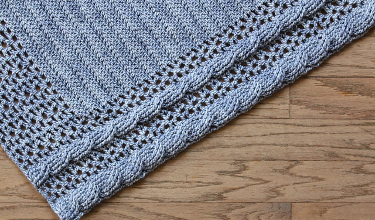 Gray crocheted fabric with intricate patterns on a wooden surface.