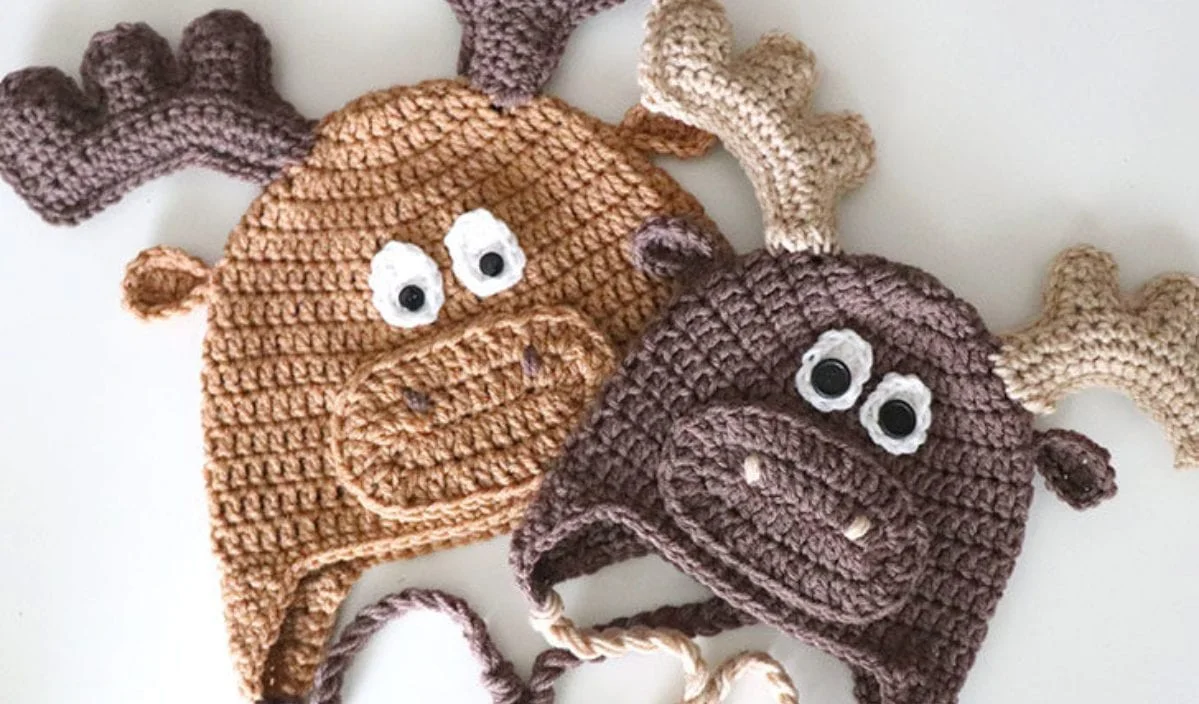 Two adorable crocheted moose hats with playful antlers and big eyes, one in brown and the other in tan, displayed on a white background. Perfect for chilly days, these winter hats come with free crochet patterns to keep you warm in style.