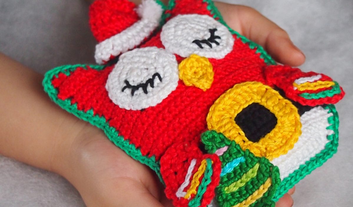 A child holds an adorable red owl softie, beautifully crocheted with a Santa hat, yellow beak, and colorful wings—a perfect showcase of delightful crochet patterns.