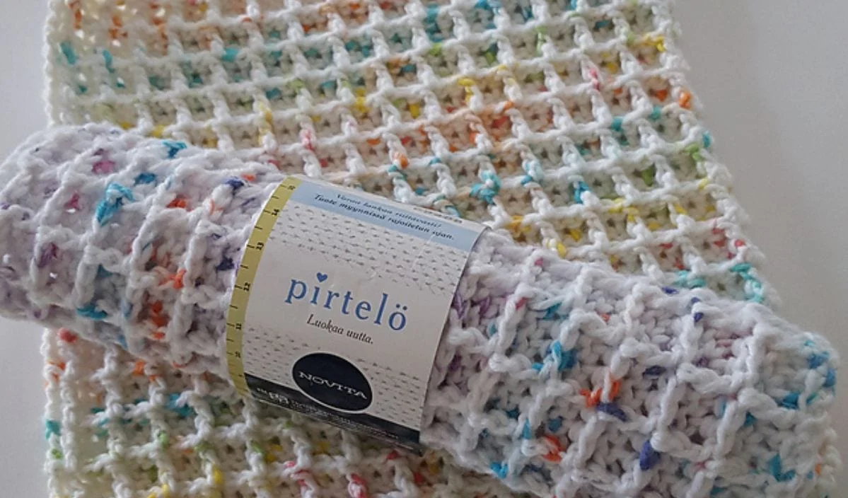 Rolled multicolored knitted blanket with a label, resting atop a similar spread-out blanket that boasts a waffle texture pattern. Perfect for those who love exploring free crochet patterns to create vibrant, textured pieces.