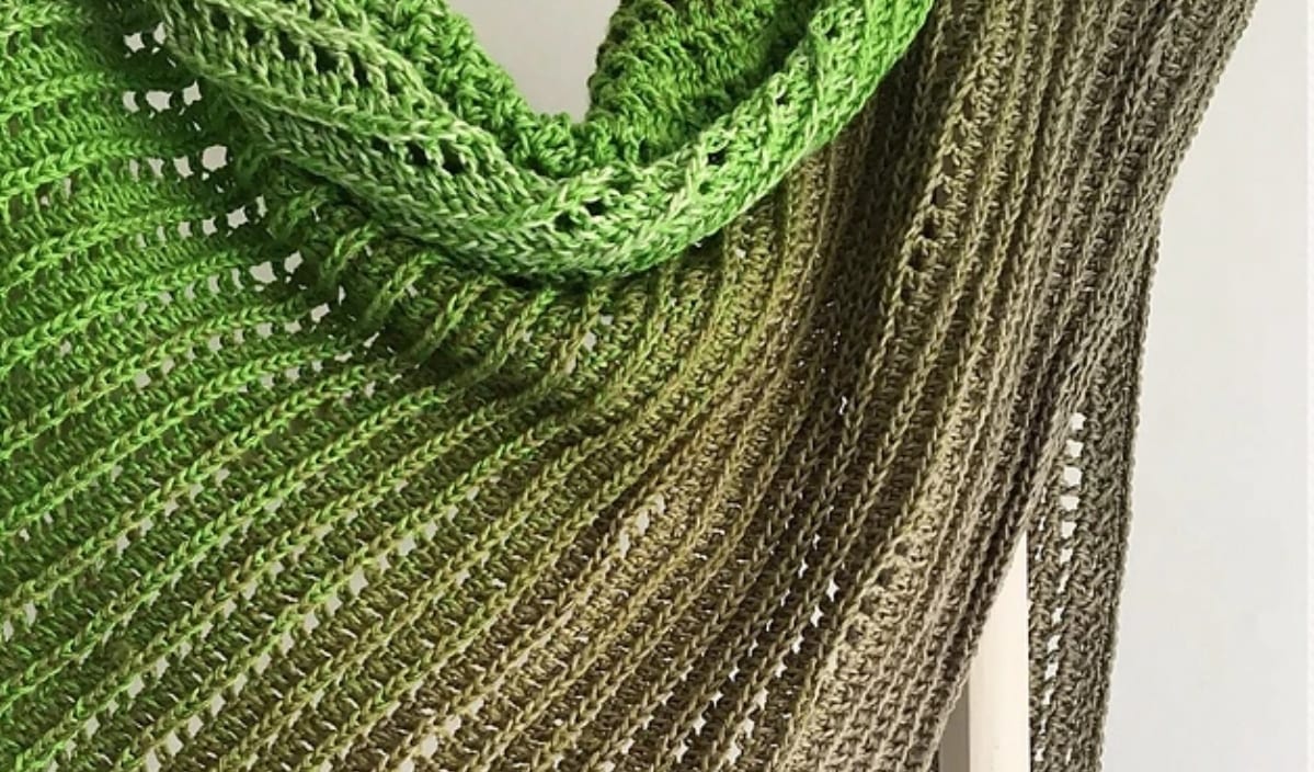 Green and brown knitted shawl with a ribbed pattern, draped neatly, perfect for layering on chilly days. Pair it with a cozy winter hat for complete warmth.