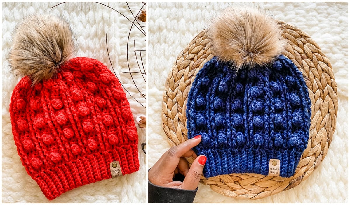 Two knitted beanies with pom-poms: one red and one blue, rest on a woven mat. A hand holds the blue beanie, which features a label on its brim. Perfect for those who love creative crochet patterns.