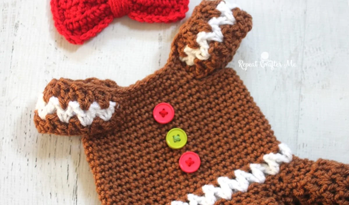 Festive crocheted gingerbread-themed outfit featuring vibrant red, green, and yellow buttons, complemented by a charming red bow, all displayed on a light wooden surface. Ideal for those seeking creative inspiration, this ensemble evokes holiday cheer with its delightful crochet patterns.