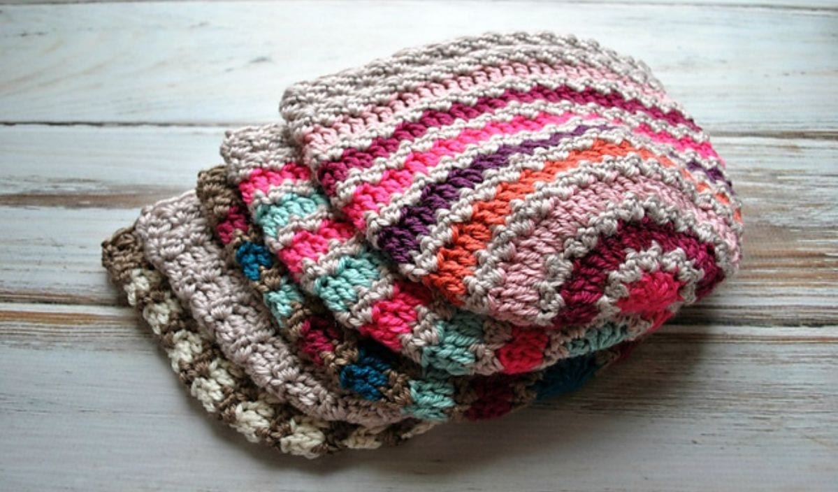 A stack of colorful, striped beanies crafted from free crochet patterns is artfully displayed on a wooden surface.