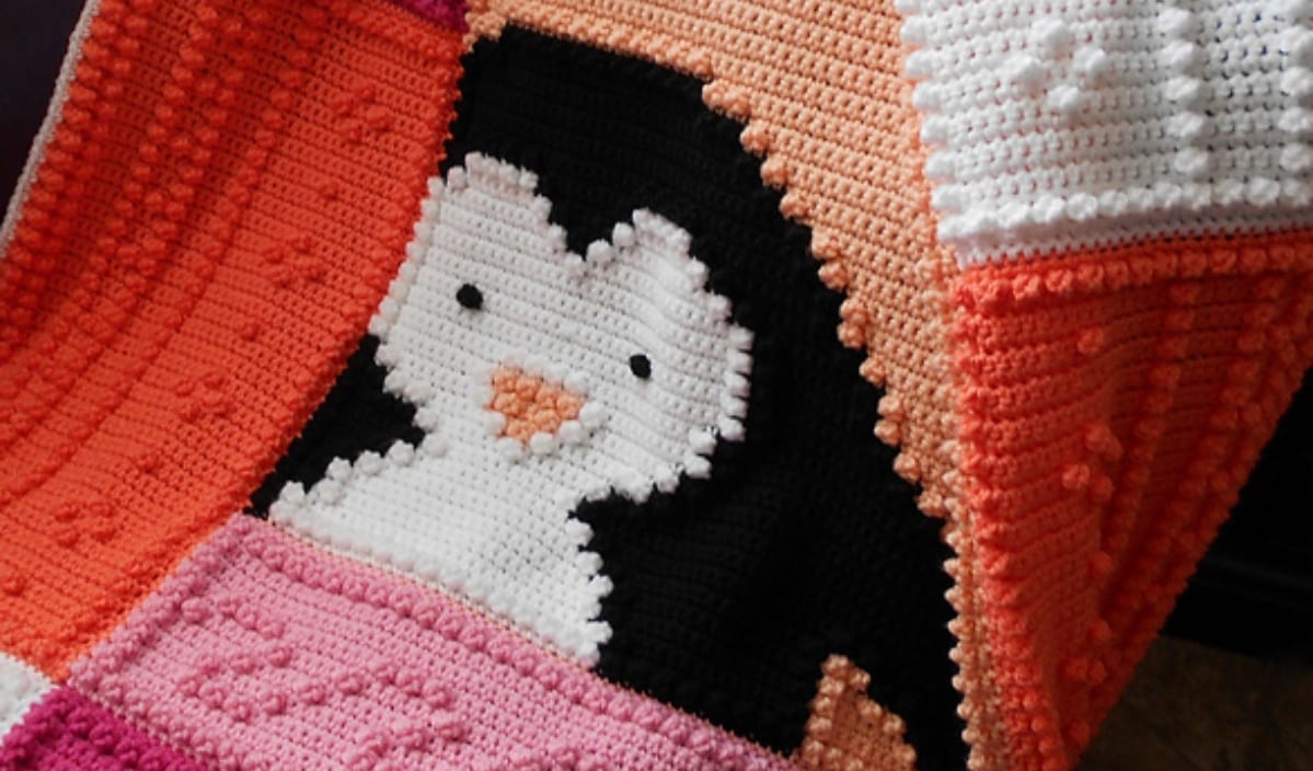 A crocheted blanket showcasing a whimsical penguin design, nestled among vibrant orange and pink sections, is an eye-catching addition to any room. This delightful piece is perfect for those who cherish unique crochet patterns in their collection.