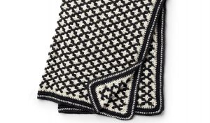 This black and white crocheted blanket features a striking star-like design, showcasing intricate crochet patterns with a geometric flair.