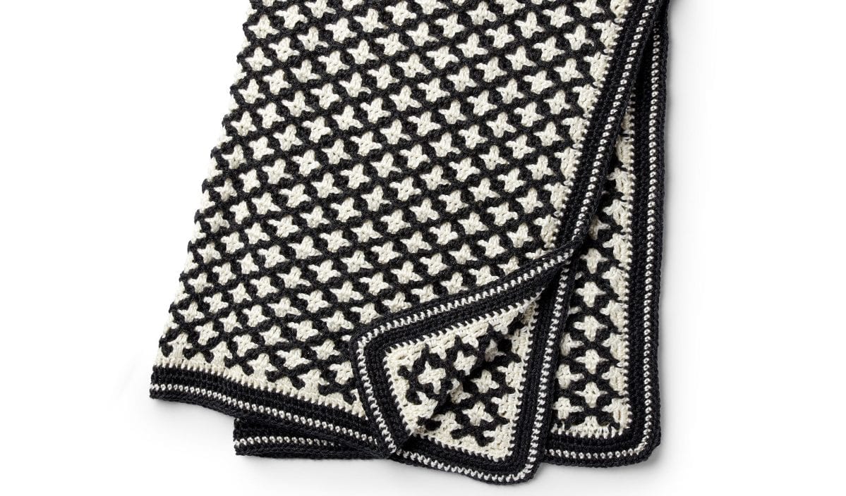 This black and white crocheted blanket features a striking star-like design, showcasing intricate crochet patterns with a geometric flair.