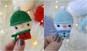 Two charming crocheted snowman ornaments: one with a green hat and red scarf, the other with a blue hat and scarf, held by a hand.背景に編み糸と温かいライトがあります。These delightful creations are perfect examples of amigurumi craftsmanship.