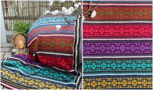 Colorful woven textiles with intricate patterns in rows of red, blue, green, purple, and yellow resemble a mosaic blanket. A branch with white flowers and a small statue grace the background.