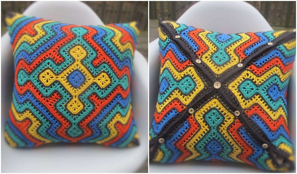 Two images of a colorful crochet pillow showcase its charm. The front boasts an intricate geometric pattern, reminiscent of detailed crochet patterns, while the back reveals a buttoned closure with a diagonal stripe design. Perfect for adding a handmade touch to any space.