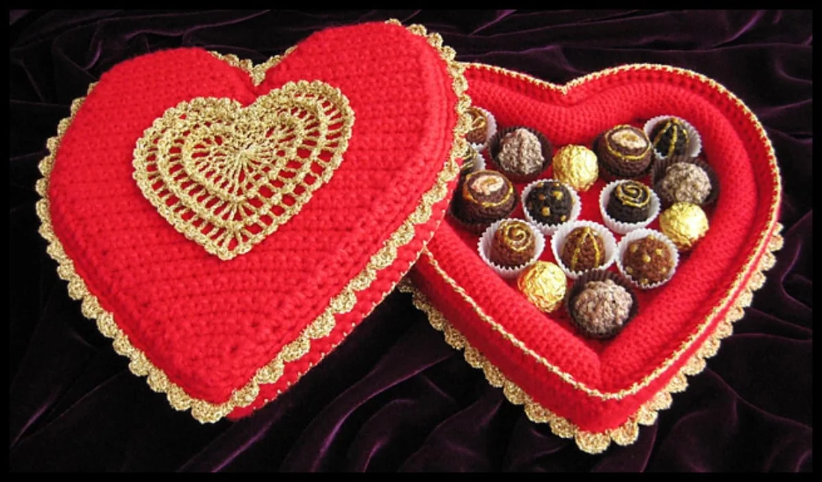 A heart-shaped crochet box with gold details contains assorted chocolates, making it a perfect Valentine's Day gift idea, elegantly displayed on a dark velvet surface.