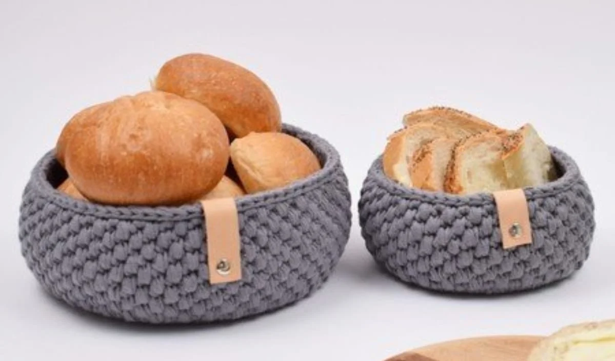 Two gray woven bread baskets with leather details; one holds round bread rolls, the other holds sliced bread.