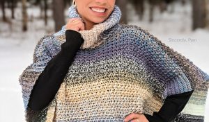 A woman beams warmly, wrapped in a multicolored knit poncho inspired by free crochet patterns, standing against the backdrop of a snowy forest.