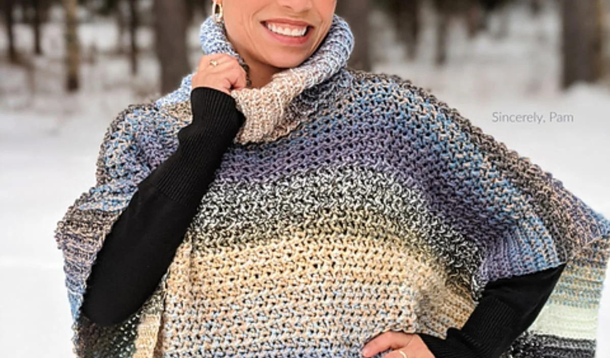 A woman beams warmly, wrapped in a multicolored knit poncho inspired by free crochet patterns, standing against the backdrop of a snowy forest.