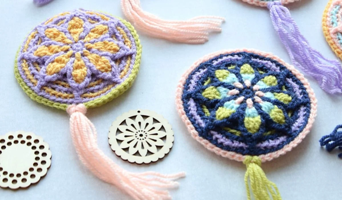 Crocheted mandalas in blue and yellow with tassels, alongside wooden circular cutouts, create a charming display. Incorporate free crochet patterns to recreate this design on a white surface for a personal touch.