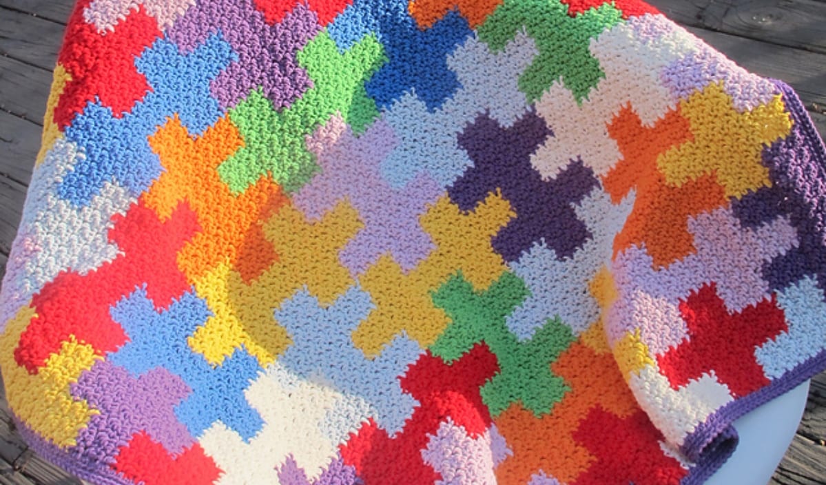 A colorful, hand-crocheted blanket featuring interlocking geometric patterns in various bright colors, crafted from free crochet patterns, is beautifully displayed on a white chair.