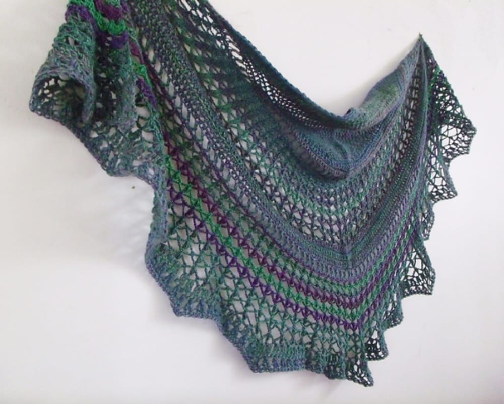 A green and purple crocheted shawl hanging on a wall.