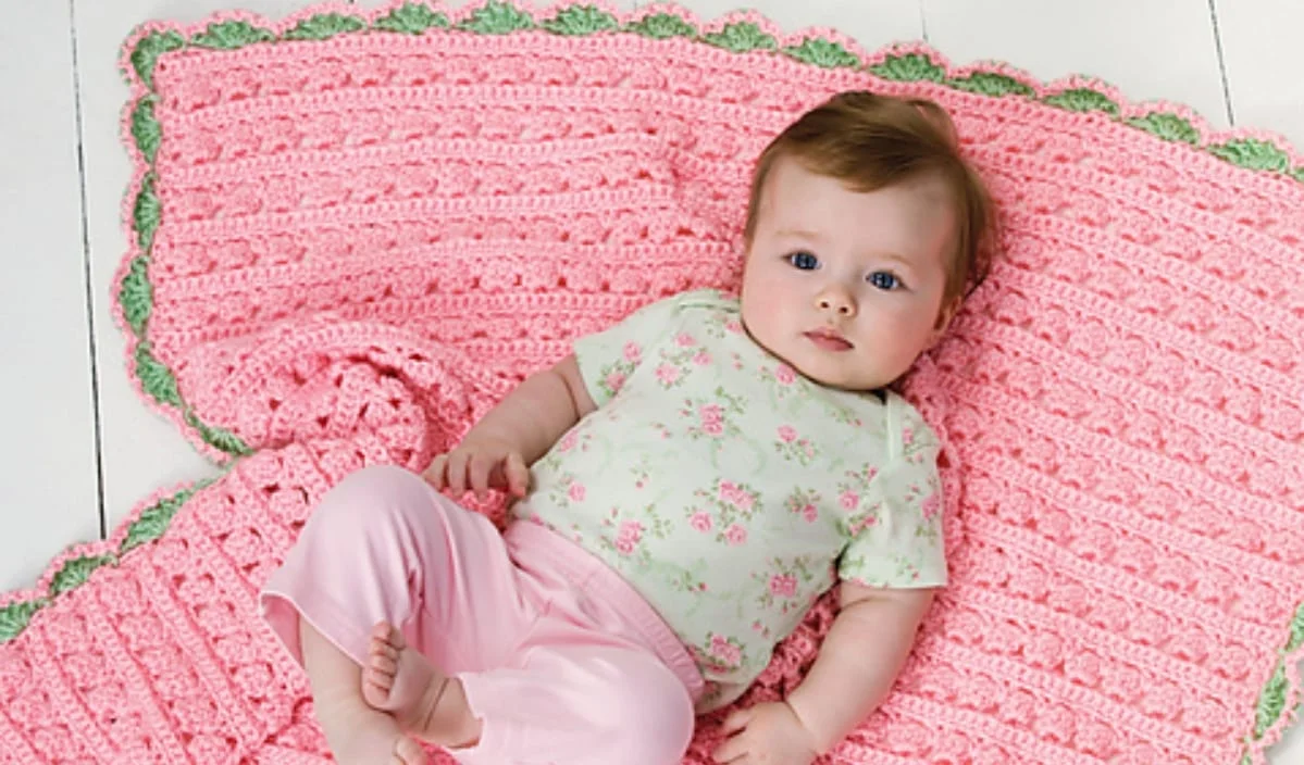 A baby wearing pink pants and a floral shirt lies on a delightful summer baby blanket, adding a pop of color to the scene.