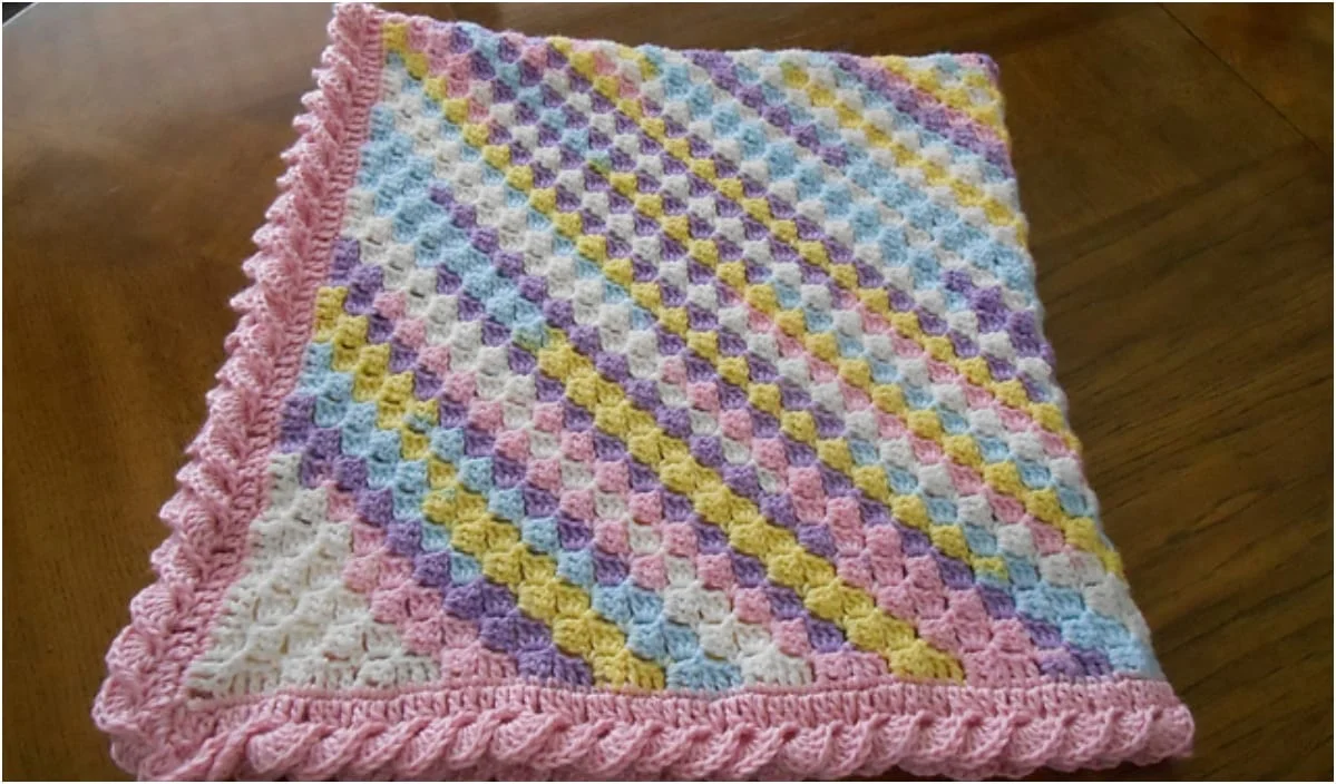 C2C baby blanket with diagonal pastel stripes and a pink scalloped edge, evoking Baby Sweet Dreams, displayed on a wooden surface.