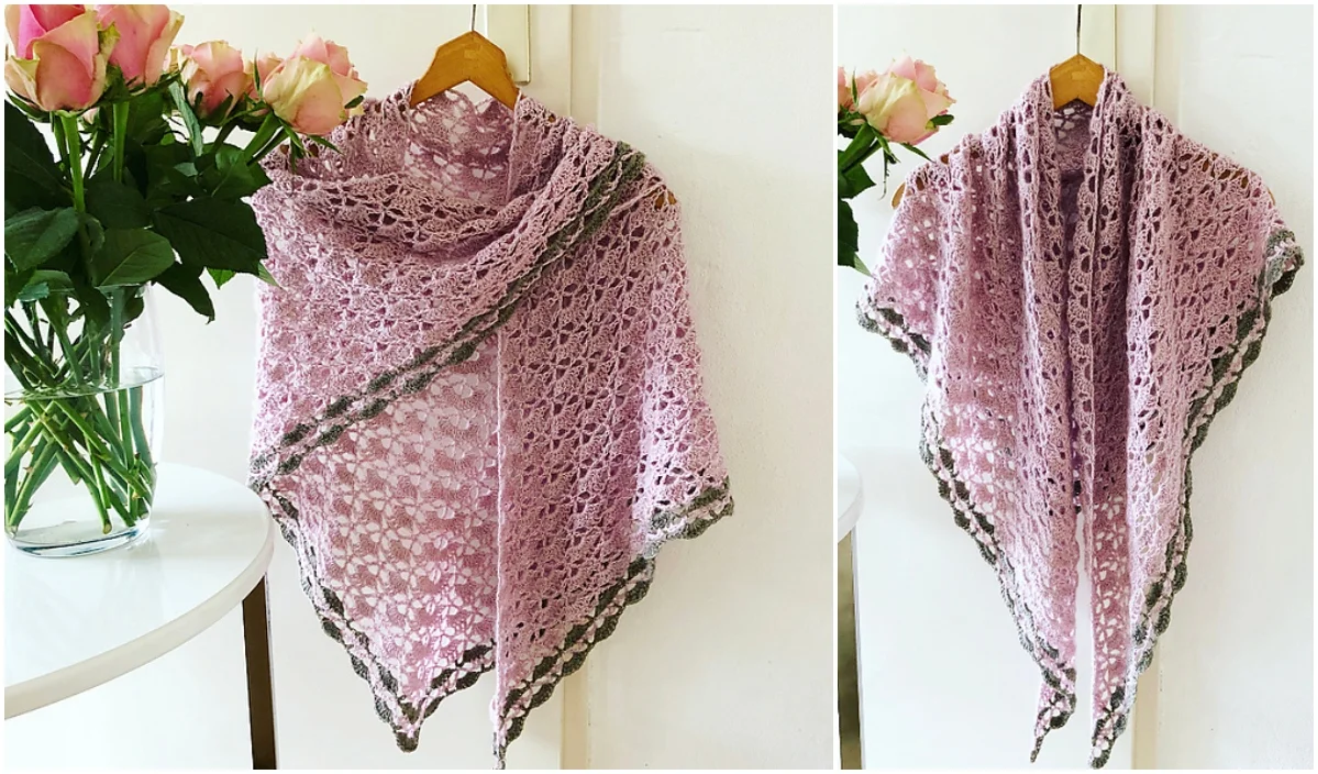 A crocheted pink shawl with green edging, featuring a delicate lace motif, hangs on a wooden hanger. Nearby, a vase holds pink roses.