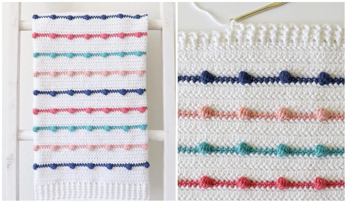 A white crocheted bobble baby blanket features rows of small, colorful bobbles in blue, pink, green, and coral. Displayed folded and close-up, this cozy creation highlights the intricate bobble stitch detailing perfect for a baby's delicate touch.