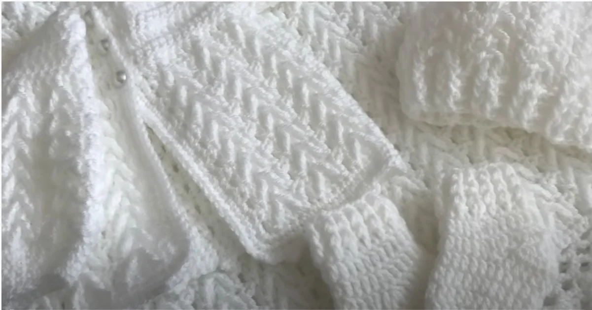 Close-up of a white crochet baby set featuring knit clothing with a textured pattern, including a sweater sleeve and hat.