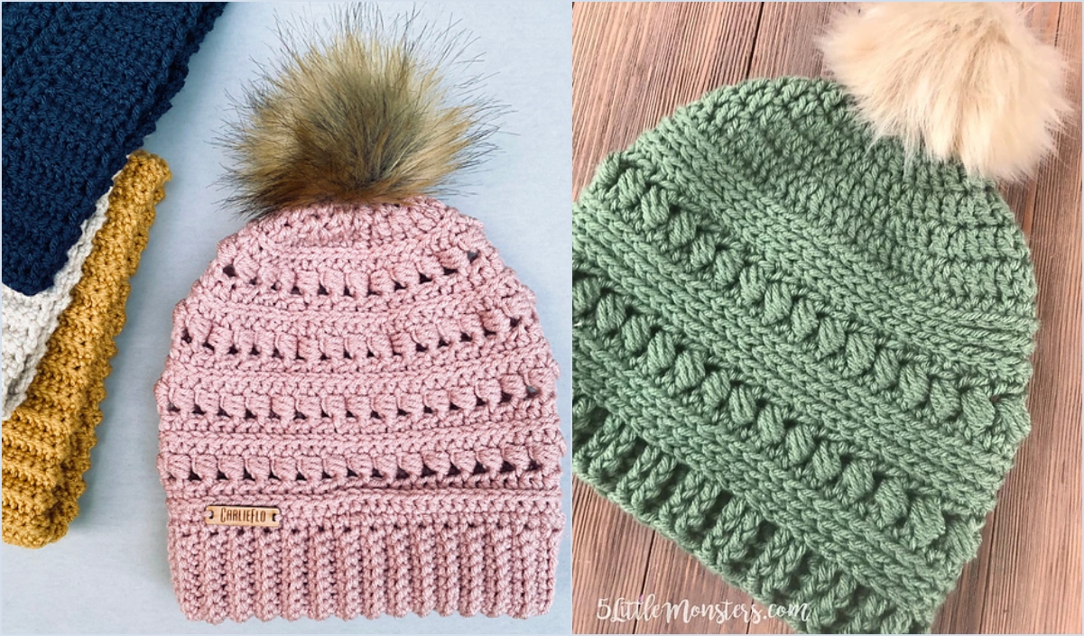 Two crocheted beanies with pom-poms; one pink with a faux fur pom-pom, the other green, crafted in a bead stitch pattern. They are displayed on a wooden surface with additional crocheted items partially visible.