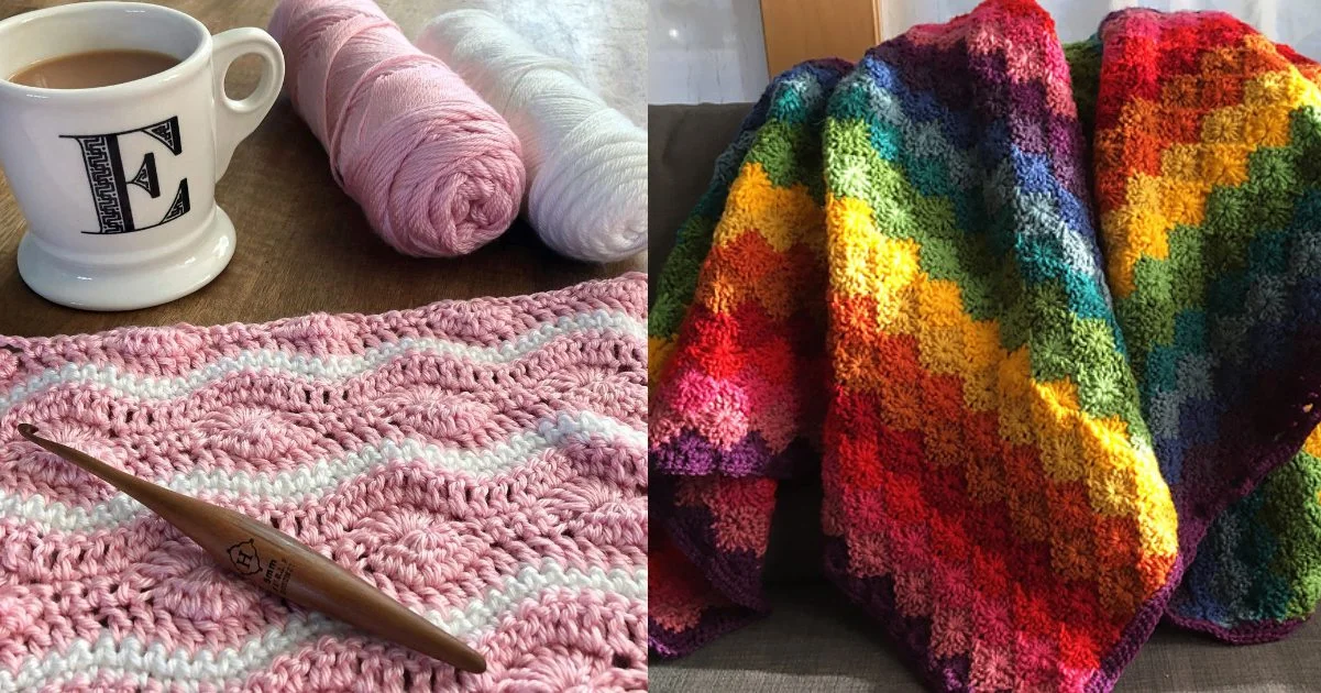 A crochet hook with pink and white yarn sits beside a mug, while a beautiful Catherine's Wheel Stitch Blanket, bursting with rainbow colors, adorns the couch.