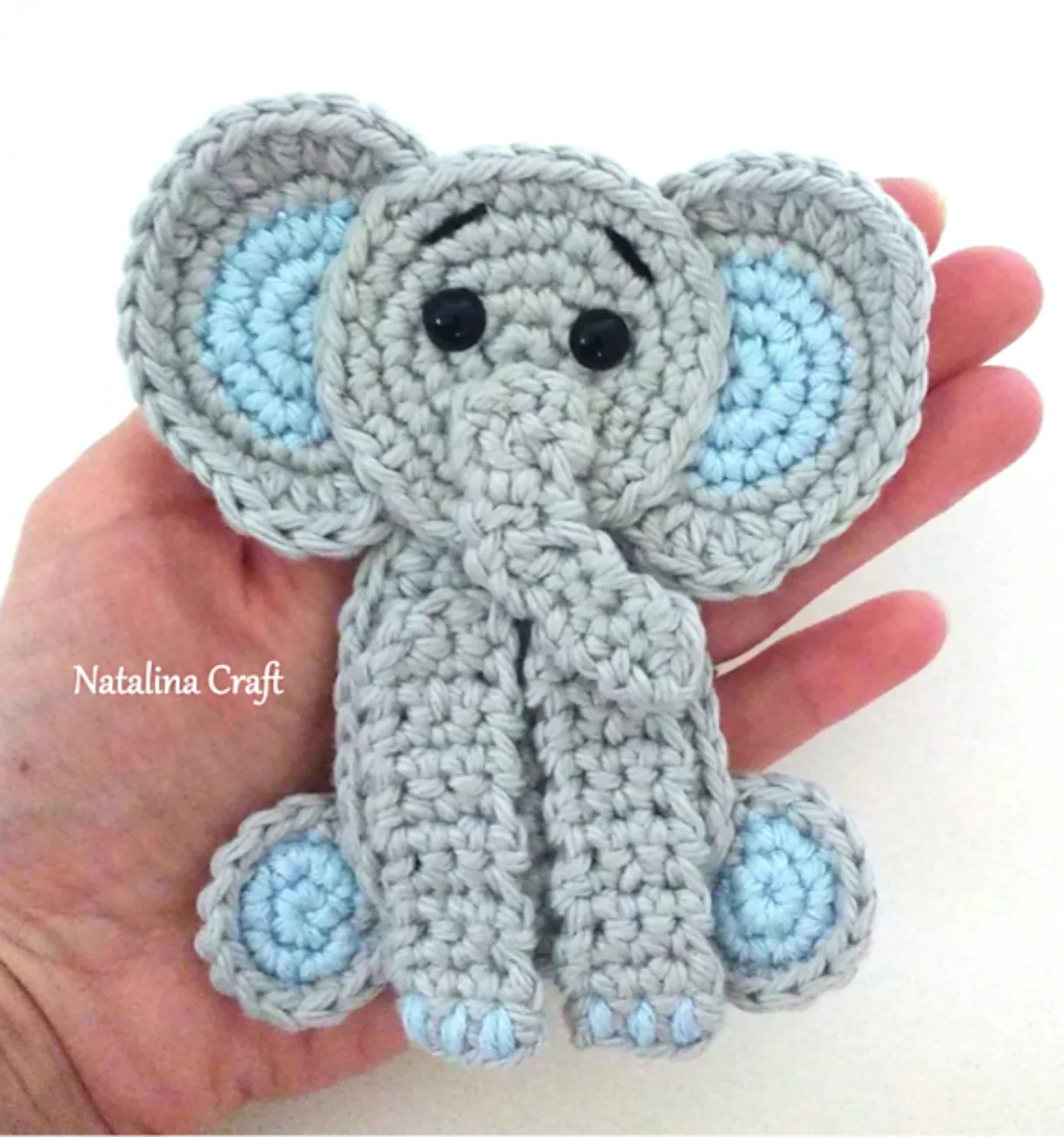 A hand holding a grey and light blue crochet elephant appliqué.
