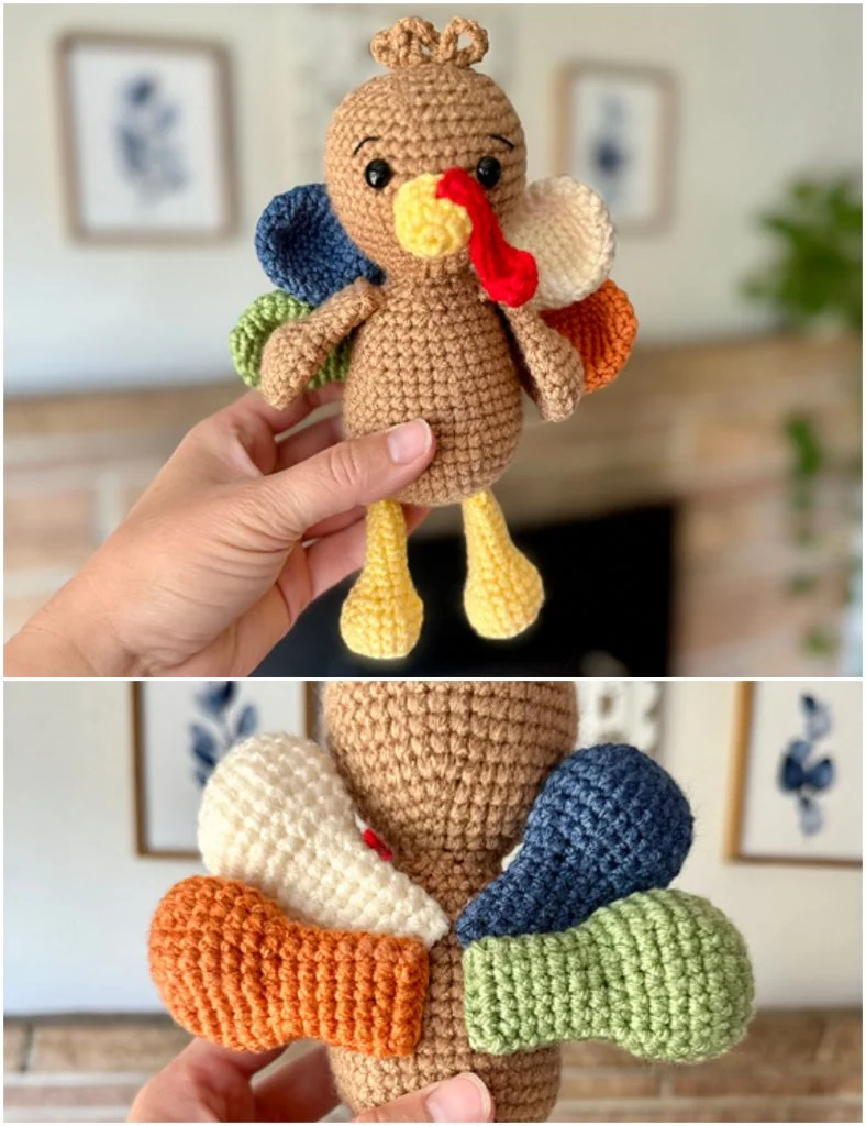 A hand holds an adorable amigurumi turkey with yellow legs and multicolored tail feathers in front of a blurred room background.