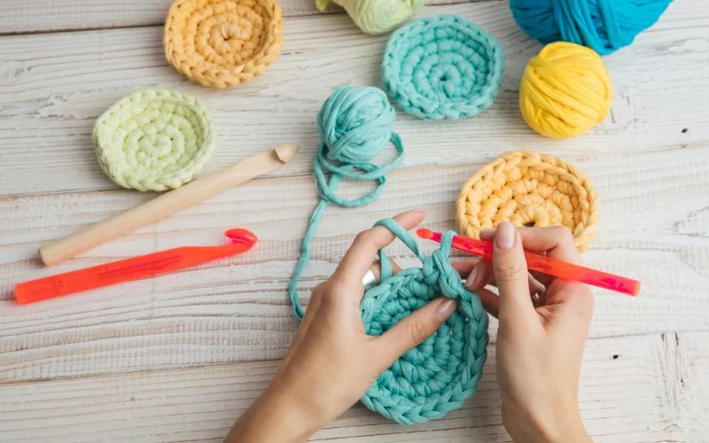 Hands skillfully crocheting with colorful yarn and tools on a wooden surface, employing clever crochet hacks to create intricate patterns effortlessly.