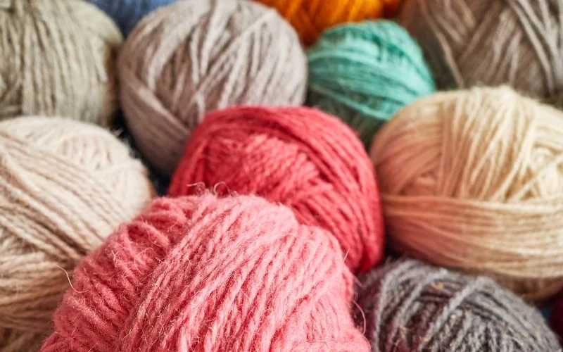 Clusters of the best yarn for blankets, featuring shades of pink, beige, green, and gray, create a colorful tapestry.