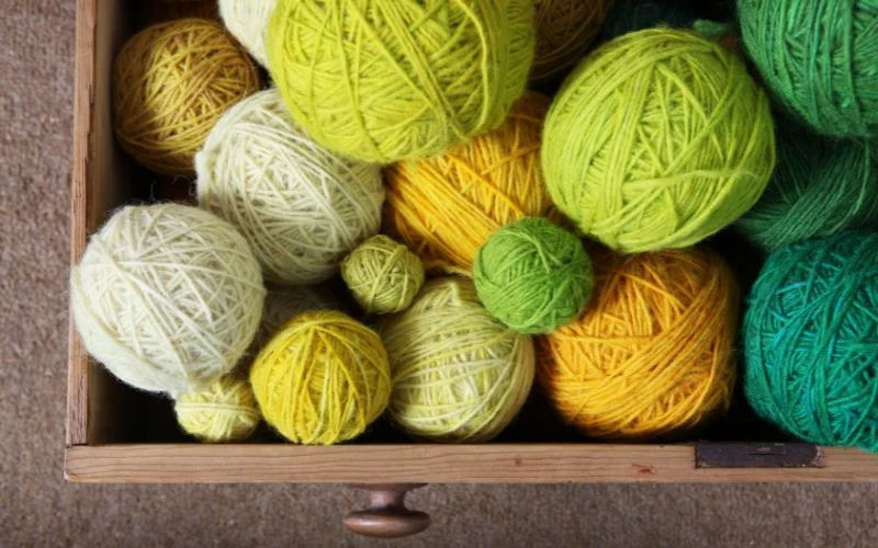 A drawer filled with the best yarn for blankets showcases balls in various shades of green, yellow, and white.