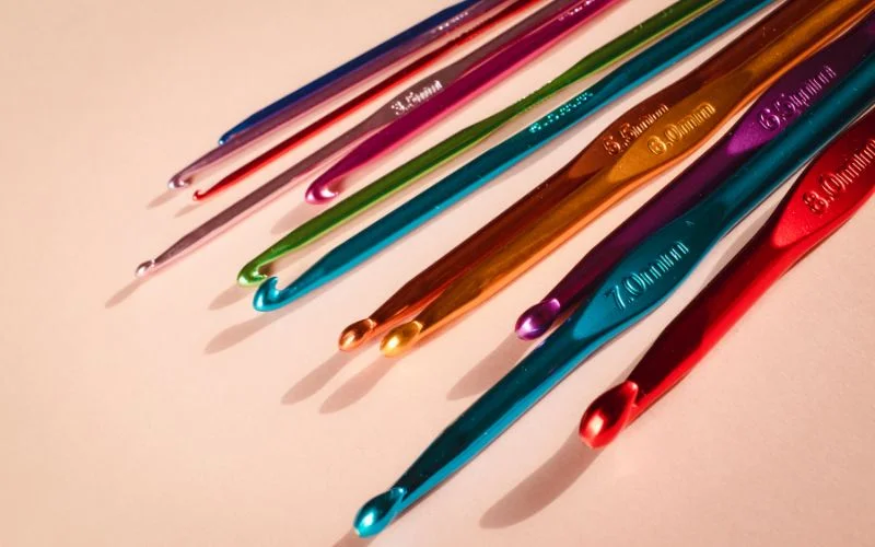 Colorful crochet hooks of varying sizes arranged diagonally on a white background, creating a visual crochet hook size chart.